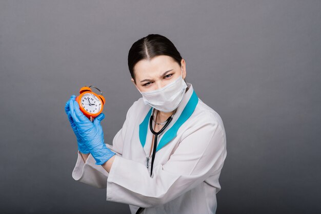 Femme médecin souriante en masque pointant sur l'horloge, l'heure de la vaccination