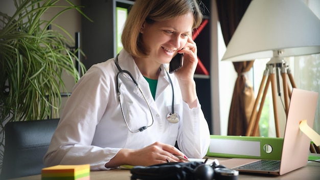 Femme médecin souriante parlant au téléphone sur le lieu de travail dans une clinique de consultation à distance des patients