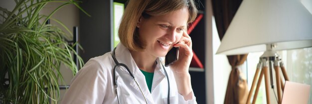 Femme médecin souriante parlant au téléphone sur le lieu de travail dans une clinique de consultation à distance des patients