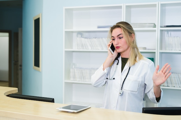 Femme médecin souriante portant un gommage et travaillant à la réception de l'hôpital