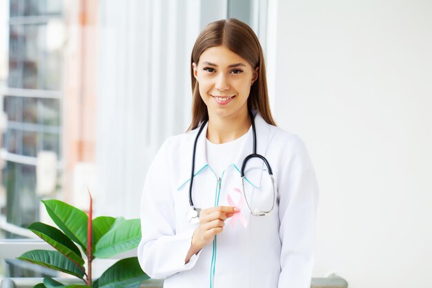 Femme médecin souriante avec ruban rose de sensibilisation au cancer dans le cabinet de l'hôpital.