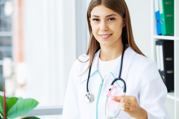 Femme médecin souriante avec ruban rose de sensibilisation au cancer dans le cabinet de l'hôpital.