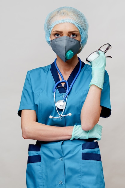 Femme médecin avec stéthoscope portant un masque de protection et des gants en latex sur fond gris clair