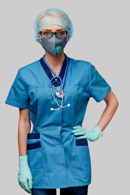 Femme médecin avec stéthoscope portant un masque de protection et des gants en latex sur un mur gris clair