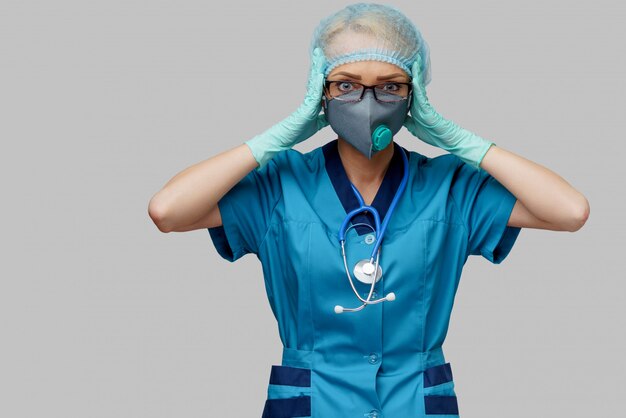 Femme médecin avec stéthoscope portant un masque de protection et des gants en latex sur un mur gris clair