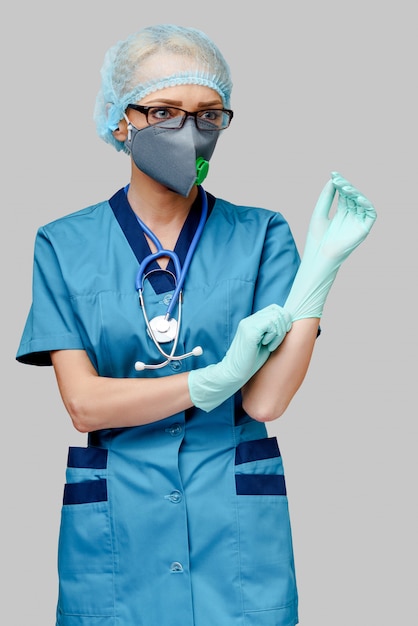 Femme médecin avec stéthoscope portant un masque de protection et des gants en latex sur un mur gris clair