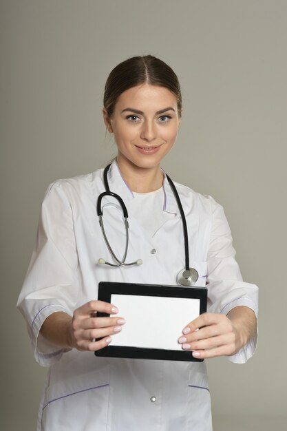 Femme médecin avec tablet pc, debout sur fond gris