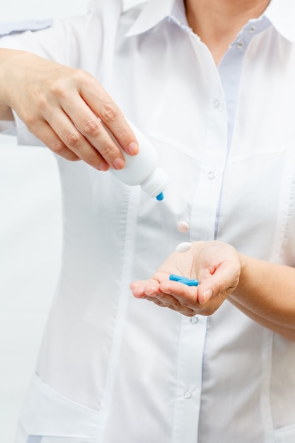 Femme médecin tenant un pot et offrant des pilules. Les comprimés tombent du flacon. Mise au point sélective sur les pilules