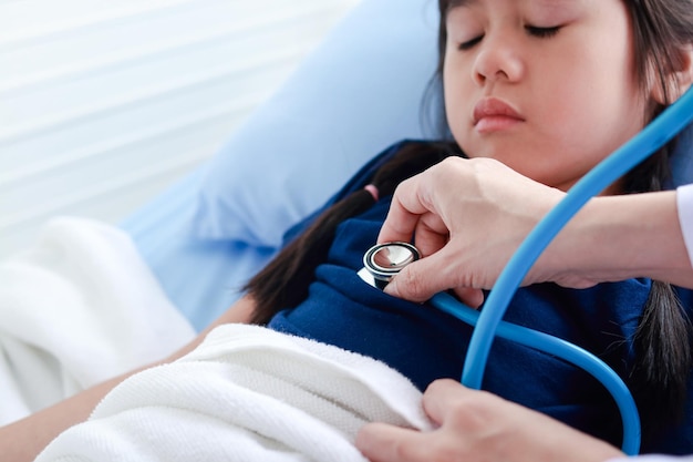 Femme médecin tenant un stéthoscope pour vérifier le pouls du rythme cardiaque d'une jolie petite fille qui dort dans son lit. Concept de service médical hospitalier, bilan de santé du jeune enfant.