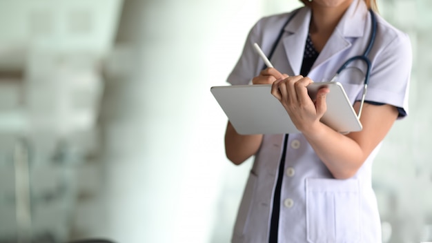 Femme médecin tenir une tablette numérique et écrire dans l&#39;écran tactile au bureau