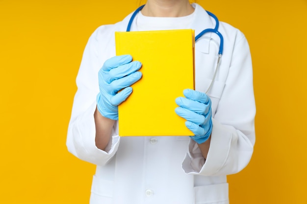 Une femme médecin tient un livre jaune sur fond jaune