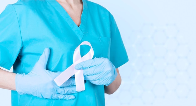 Une femme médecin en uniforme médical soutient ses seins et un ruban rose comme symbole de la sensibilisation au cancer du sein Espace de copie de fond bleu médical Photo de haute qualité