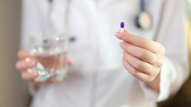 Une femme médecin en uniforme tient une capsule de vitamines et un verre d'eau dans le spécialiste des mains