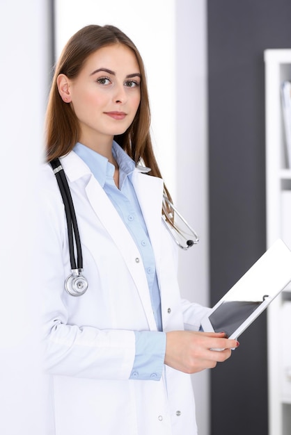 Femme médecin utilisant une tablette tout en se tenant juste près de la fenêtre à l'hôpital. Heureux médecin au travail. Concept de médecine et de soins de santé.