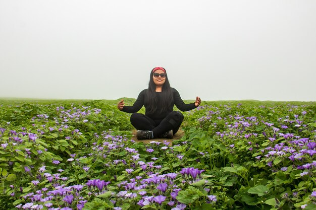 Femme méditant assise au milieu du chemin des plantes vertes fleurs lilas et ciel nuageux
