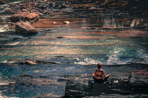 Photo une femme méditant devant une rivière avec une montagne en arrière-plan.