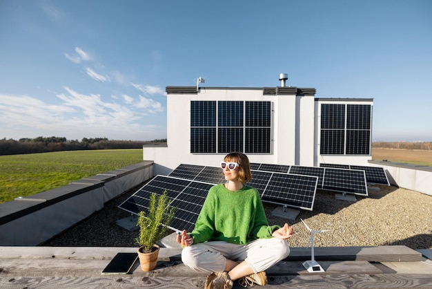 Une femme médite sur le toit de sa maison avec une centrale solaire en arrière-plan