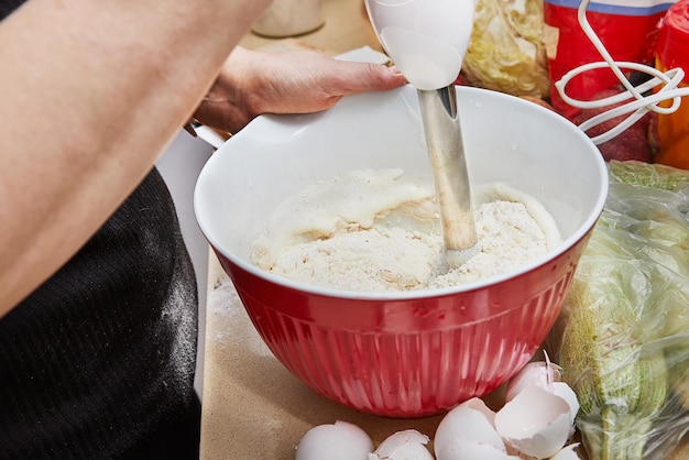 Une femme de ménage batte des crêpes dans la cuisine avec un mélangeur et un bol