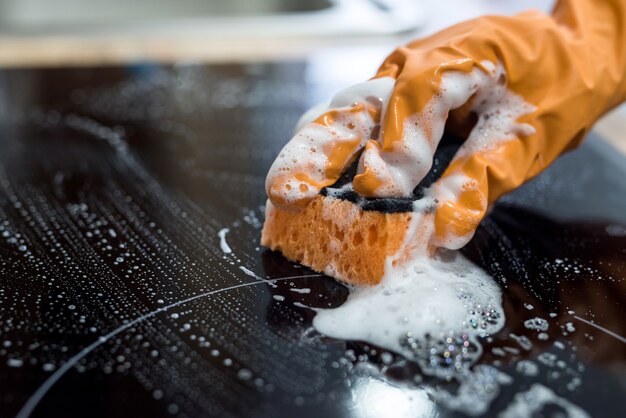 Femme de ménage nettoyant la surface du poêle en céramique moderne avec une éponge dans la cuisine