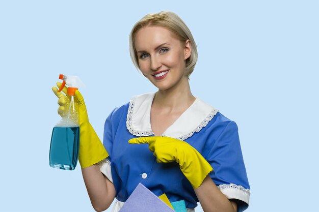 Une femme de ménage positive pointe du doigt un spray de nettoyage