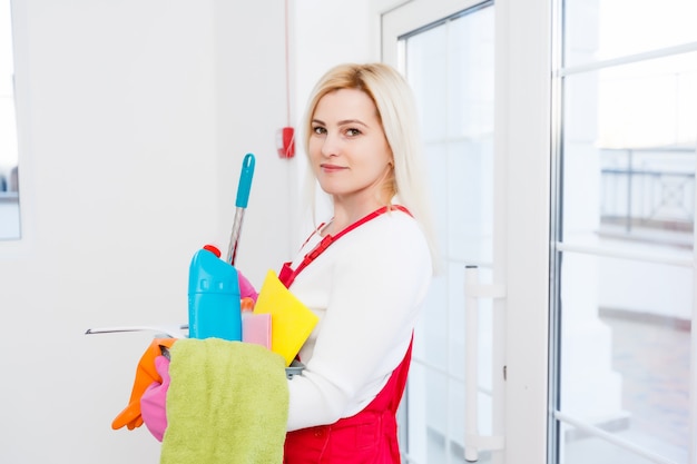 Femme de ménage avec un seau et des produits de nettoyage sur fond de bureau.