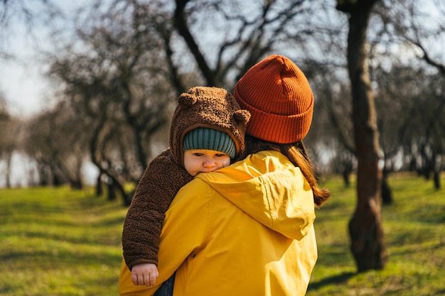 une femme mère dans un imperméable jaune dans un chapeau rouge se tient debout avec son dos et tient un enfant