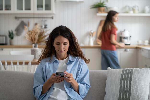 Femme mère tenant un smartphone faisant ses courses en ligne tout en passant du temps avec sa fille à la maison