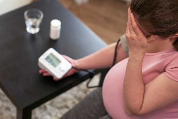 Photo une femme mesure la pression artérielle avec un manomètre électronique, des maux de tête pendant la grossesse, une mauvaise santé. se concentrer sur la main
