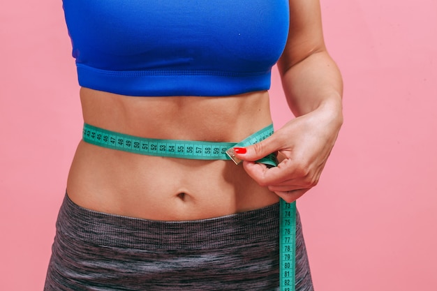 La femme mesure une taille sur un gros plan de mur rose