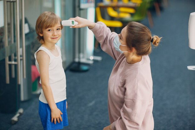 Femme de mesure de la température de l'enfant par thermomètre laser à la maternelle