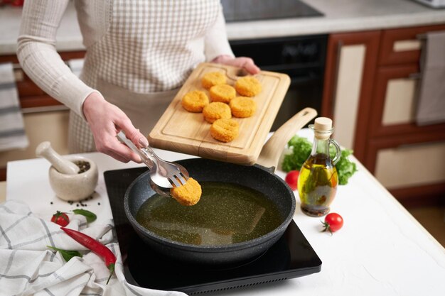 Une femme met des boulettes de fromage dans une poêle avec de l'huile de cuisson chaude