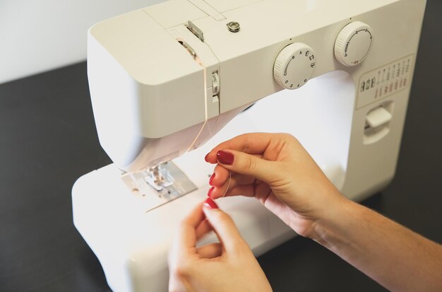 La femme met du fil dans la machine à coudre. Les mains des filles au travail indépendant. Concept de mode. Création d'un nouveau processus de vêtements. Idées de passe-temps.