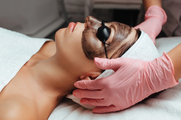 Une femme met des lunettes lors d'un rendez-vous chez un cosmétologue pour un peeling au carbone