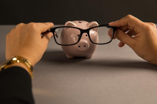 Une femme met des lunettes sur une tirelire