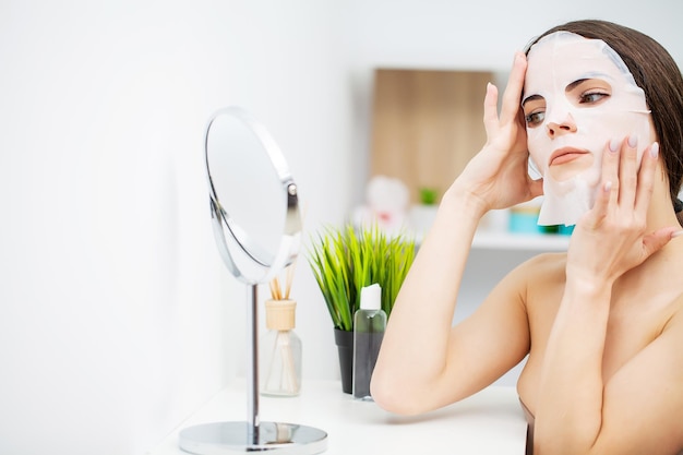 La femme met un masque facial pour les soins de la peau dans la salle de bain.