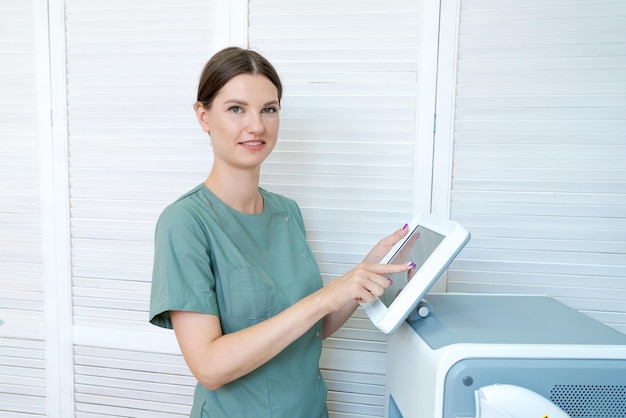 Femme met en place une machine d'épilation au laser Elle est debout en robe verte