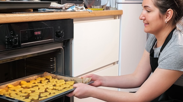 La femme met une plaque à pâtisserie avec des biscuits au four