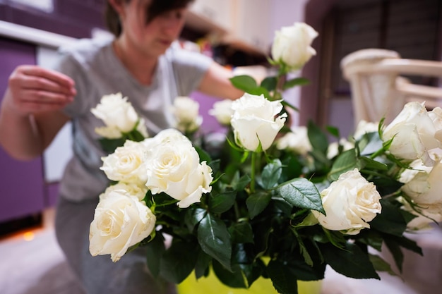 La femme met les roses blanches dans un pot vert