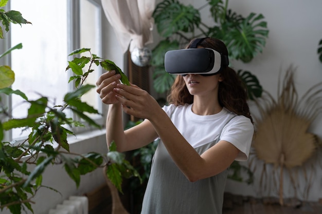 Femme de métaverse de jardinage domestique utilisant des lunettes vr dans une serre touchant la réalité augmentée des plantes