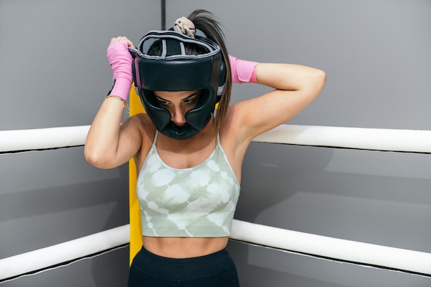 Femme mettant un casque de protection pour pratiquer le kickboxing debout dans le coin de la boxe en ring