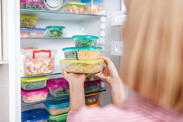 Femme mettant des conteneurs avec des légumes mélangés surgelés du congélateur.