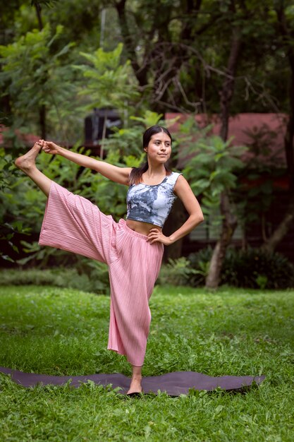 Femme mexicaine faisant du yoga avec différentes postures dans le parc extérieur avec de l'herbe et des arbres dans le bac...