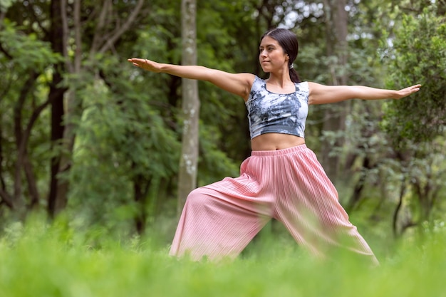 Femme mexicaine faisant du yoga avec différentes postures dans le parc extérieur avec de l'herbe et des arbres