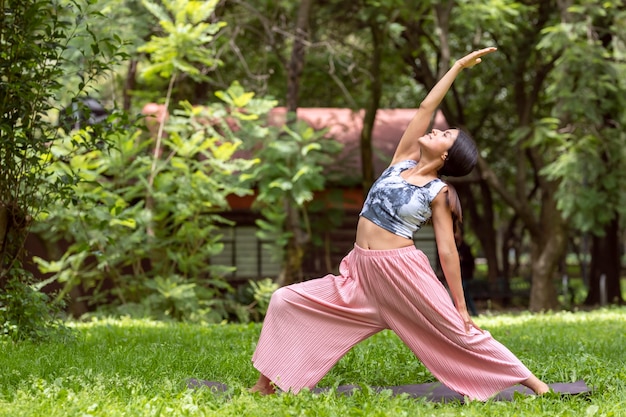 Femme mexicaine faisant du yoga avec différentes postures dans le parc extérieur avec de l'herbe et des arbres