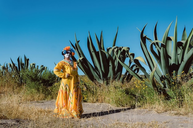 Femme mexicaine en robe colorée et maquillage de crâne dans le cactus du désert mexicain