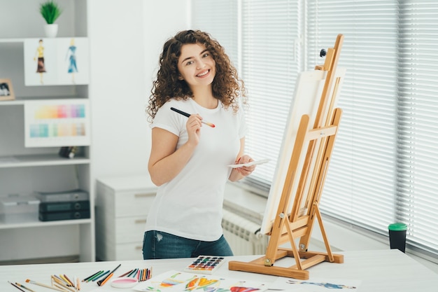 La femme mignonne avec un pinceau d'art peignant une image sur le chevalet