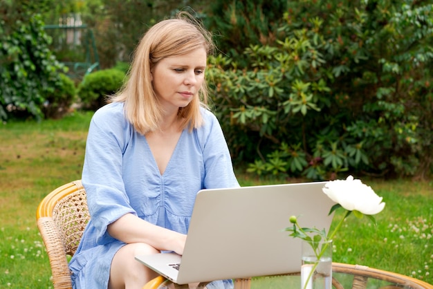 Femme mignonne réfléchie travaillant avec son ordinateur portable à table dans le parc ou le jardin