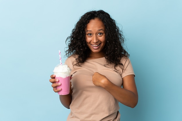 Femme avec milkshake aux fraises isolé sur bleu avec une expression faciale surprise