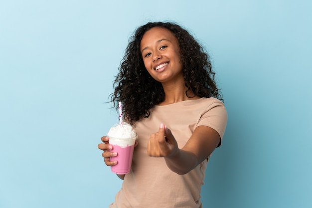 Femme avec milkshake aux fraises isolé sur bleu faisant le geste de l'argent