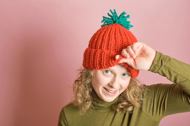 Photo une femme millénaire ludique s'amuse à porter un bonnet tricoté rouge d'hiver sur fond rose. concept de mode d'hiver